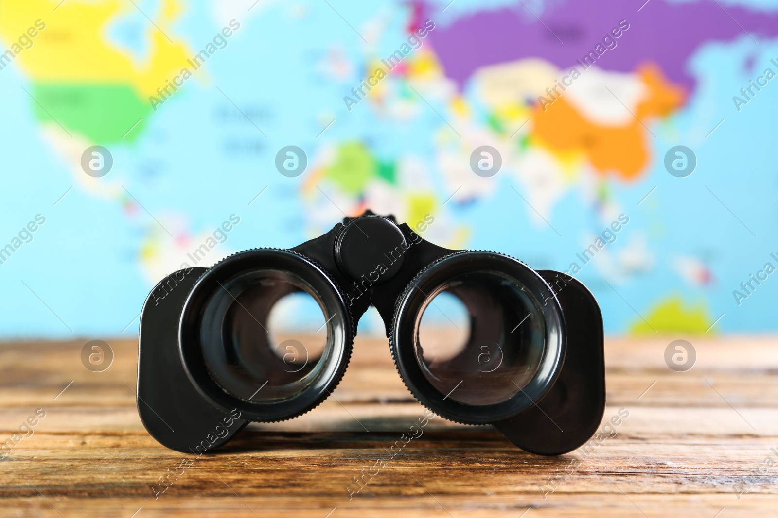 Modern binoculars on wooden table against blurred map Photo of Modern binoculars on wooden table against blurred map