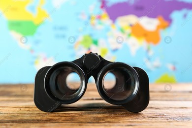 Modern binoculars on wooden table against blurred map Photo of Modern binoculars on wooden table against blurred map