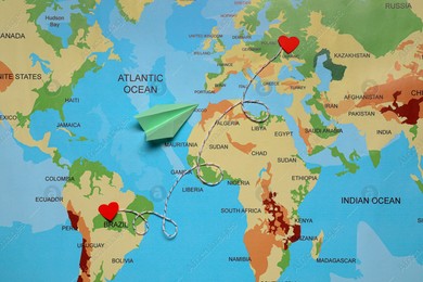 Paper plane and decorative cord between two red hearts on world map symbolizing connection in long-distance relationship, flat lay Photo of Paper plane and decorative cord between two red hearts on world map symbolizing connection in long-distance relationship, flat lay