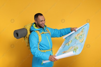 Happy tourist with backpack and map on yellow background Photo of Happy tourist with backpack and map on yellow background