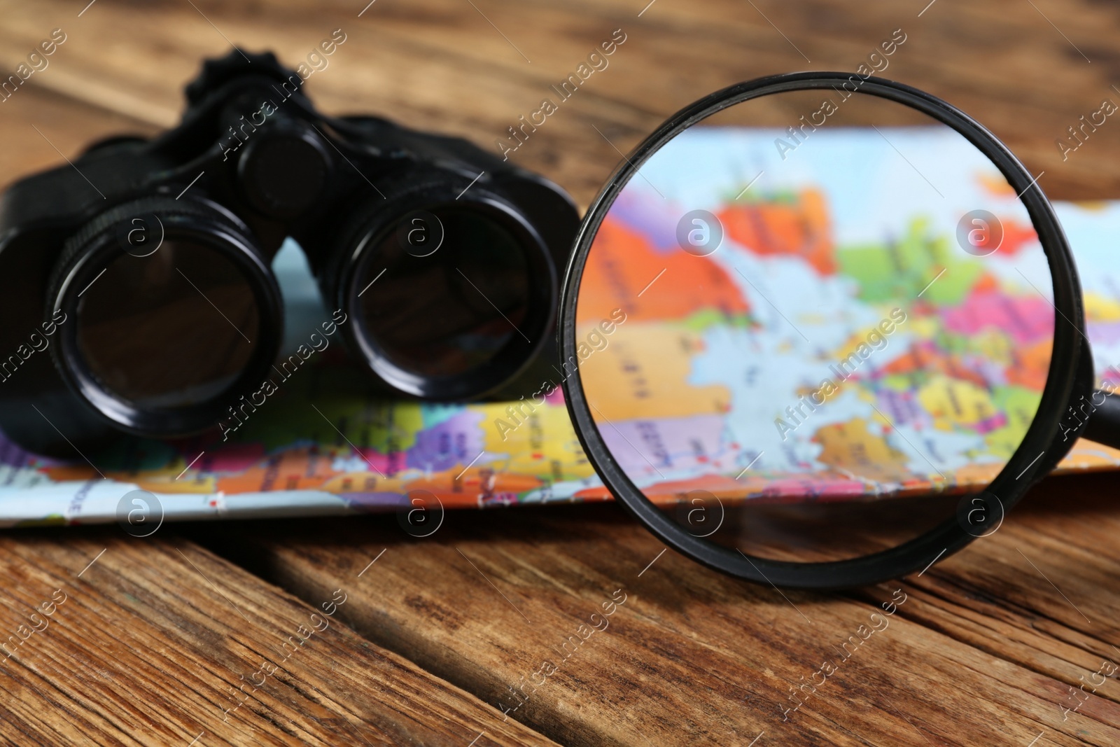 Magnifying glass, modern binoculars and map on wooden table, closeup Photo of Magnifying glass, modern binoculars and map on wooden table, closeup