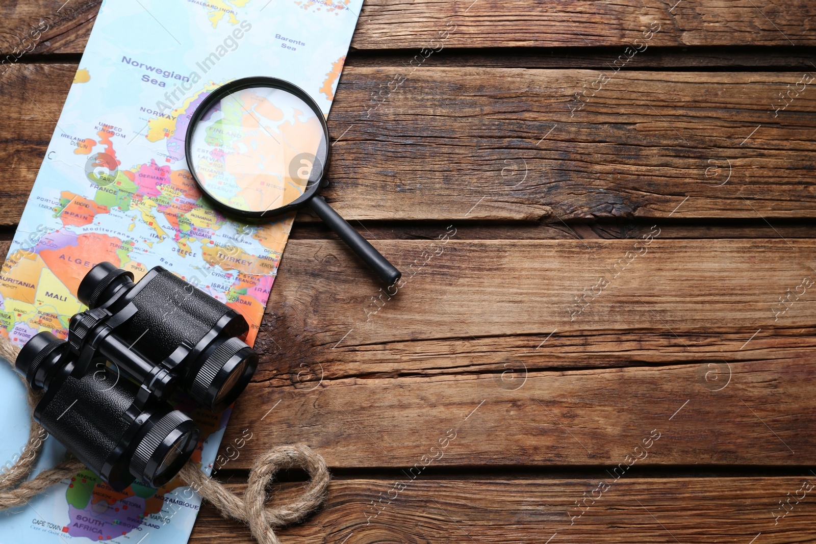 Modern binoculars, magnifying glass, map and rope on wooden table, flat lay. Space for text Photo of Modern binoculars, magnifying glass, map and rope on wooden table, flat lay. Space for text