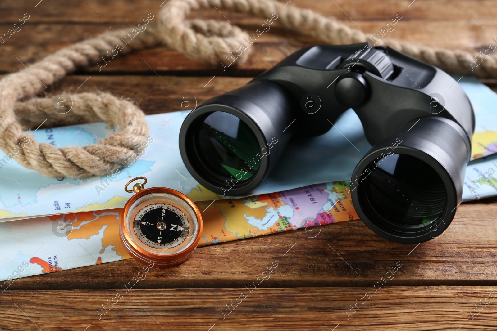 Modern binoculars, map, compass and rope on wooden table, closeup Photo of Modern binoculars, map, compass and rope on wooden table, closeup
