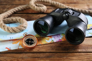 Modern binoculars, map, compass and rope on wooden table, closeup Photo of Modern binoculars, map, compass and rope on wooden table, closeup