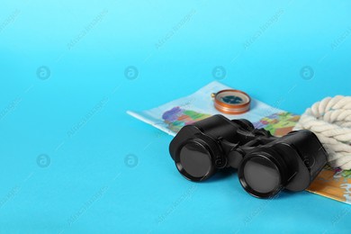Modern binoculars, rope, map and compass on light blue background, space for text Photo of Modern binoculars, rope, map and compass on light blue background, space for text
