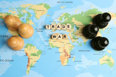 Wooden cubes with phrase Trade war and chess pieces on world map, flat lay Photo of Wooden cubes with phrase Trade war and chess pieces on world map, flat lay