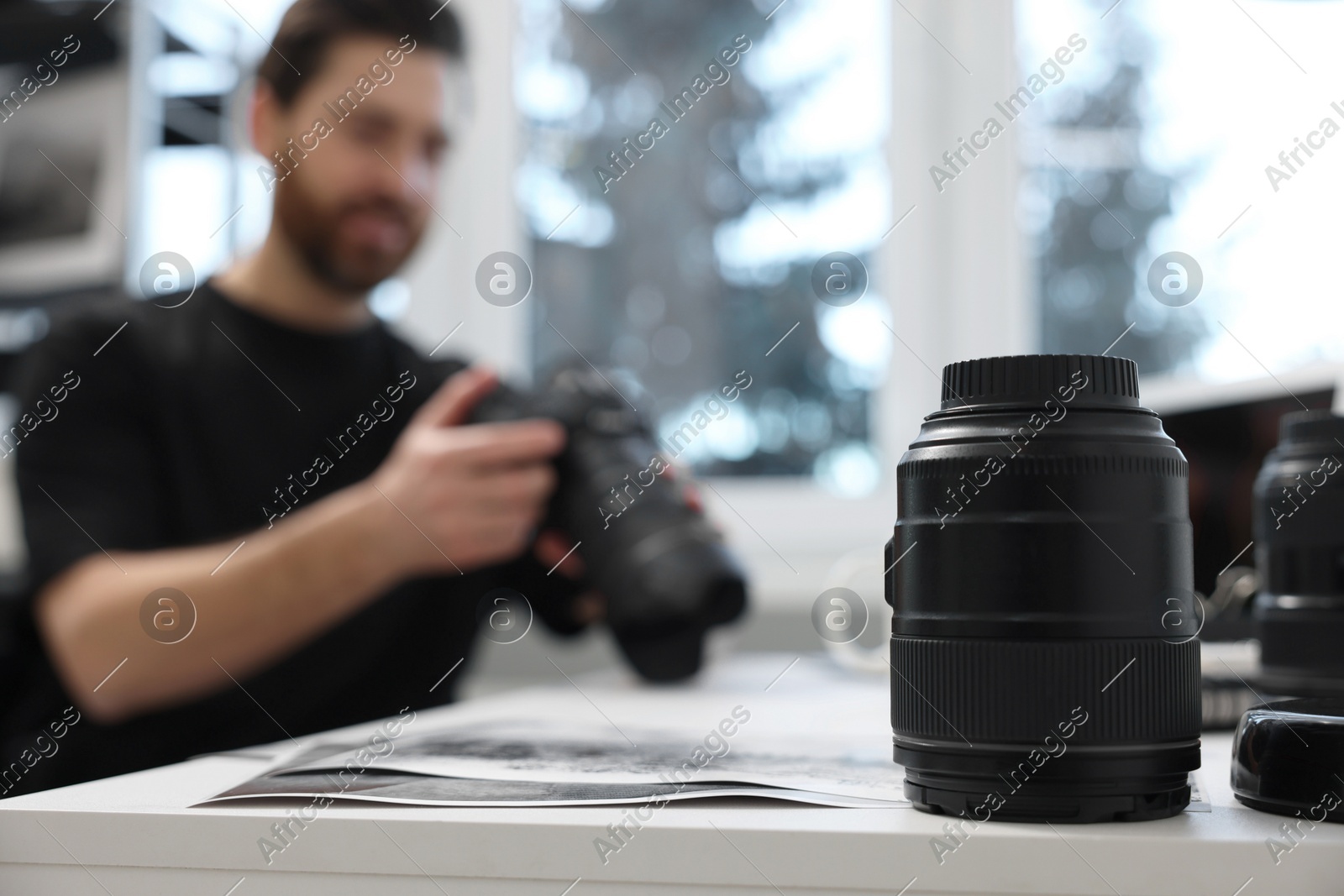 Professional photographer holding digital camera at table indoors, focus on lens Photo of Professional photographer holding digital camera at table indoors, focus on lens