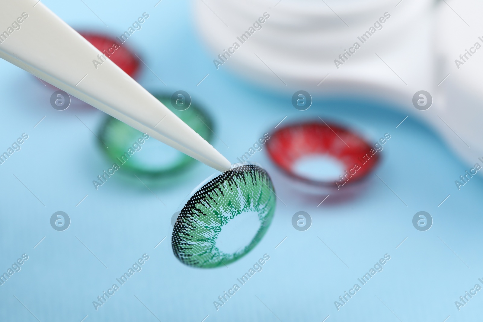 Tweezers with green contact lens on light blue background, closeup. Space for text Photo of Tweezers with green contact lens on light blue background, closeup. Space for text