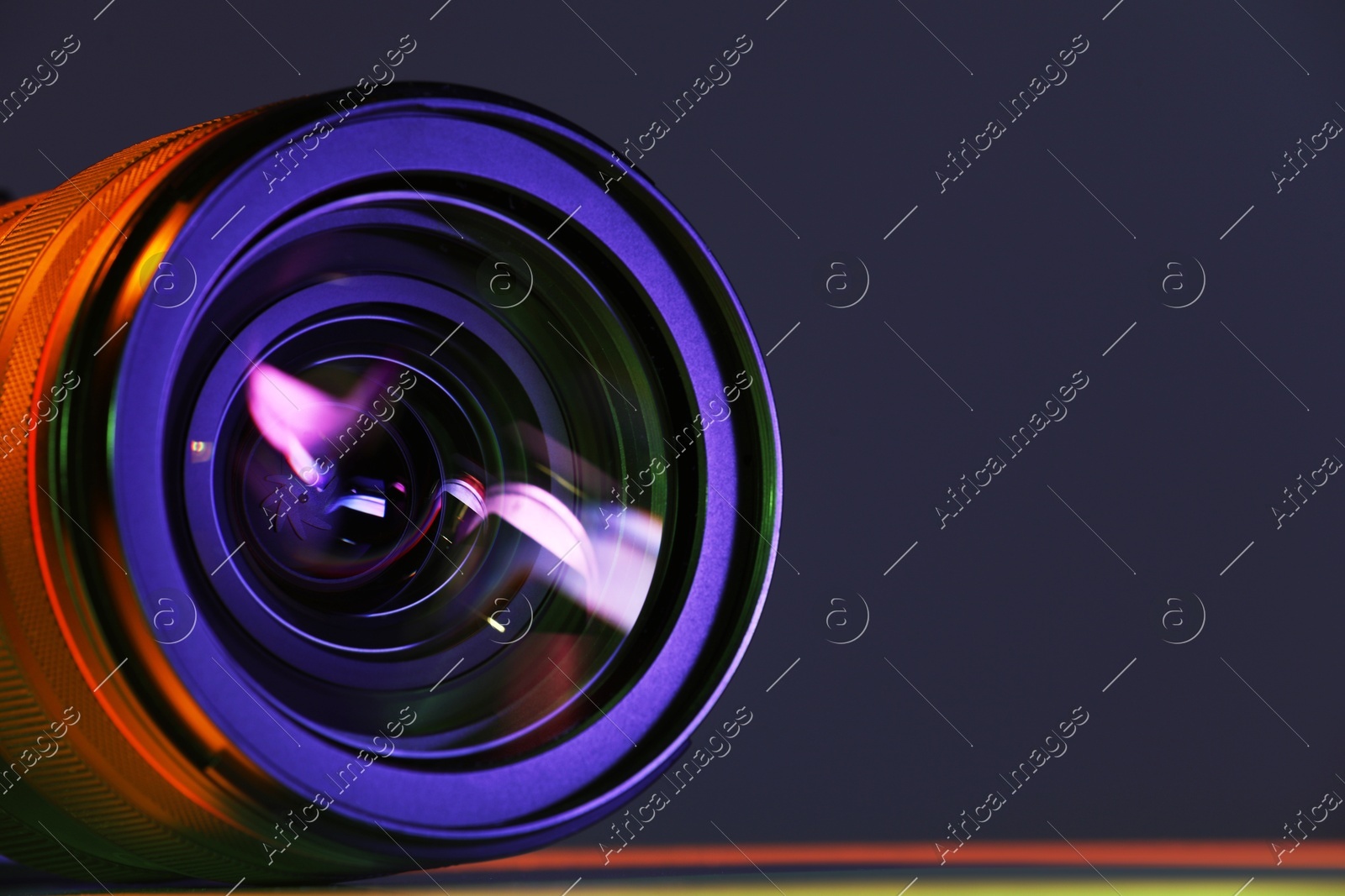 Modern camera lens in neon lights on table, closeup. Space for text Photo of Modern camera lens in neon lights on table, closeup. Space for text