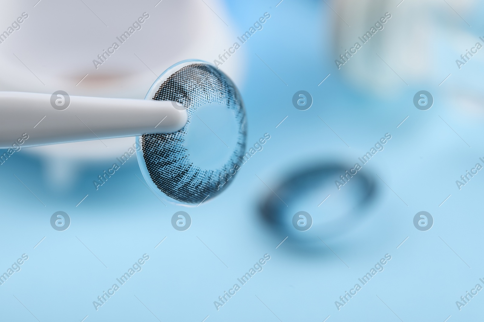 Tweezers with color contact lens on light blue background, closeup. Space for text Photo of Tweezers with color contact lens on light blue background, closeup. Space for text