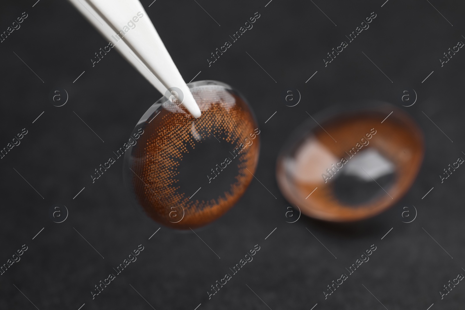 Tweezers with color contact lens on dark background, closeup. Space for text Photo of Tweezers with color contact lens on dark background, closeup. Space for text