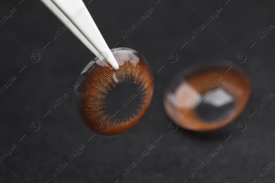 Tweezers with color contact lens on dark background, closeup. Space for text Photo of Tweezers with color contact lens on dark background, closeup. Space for text