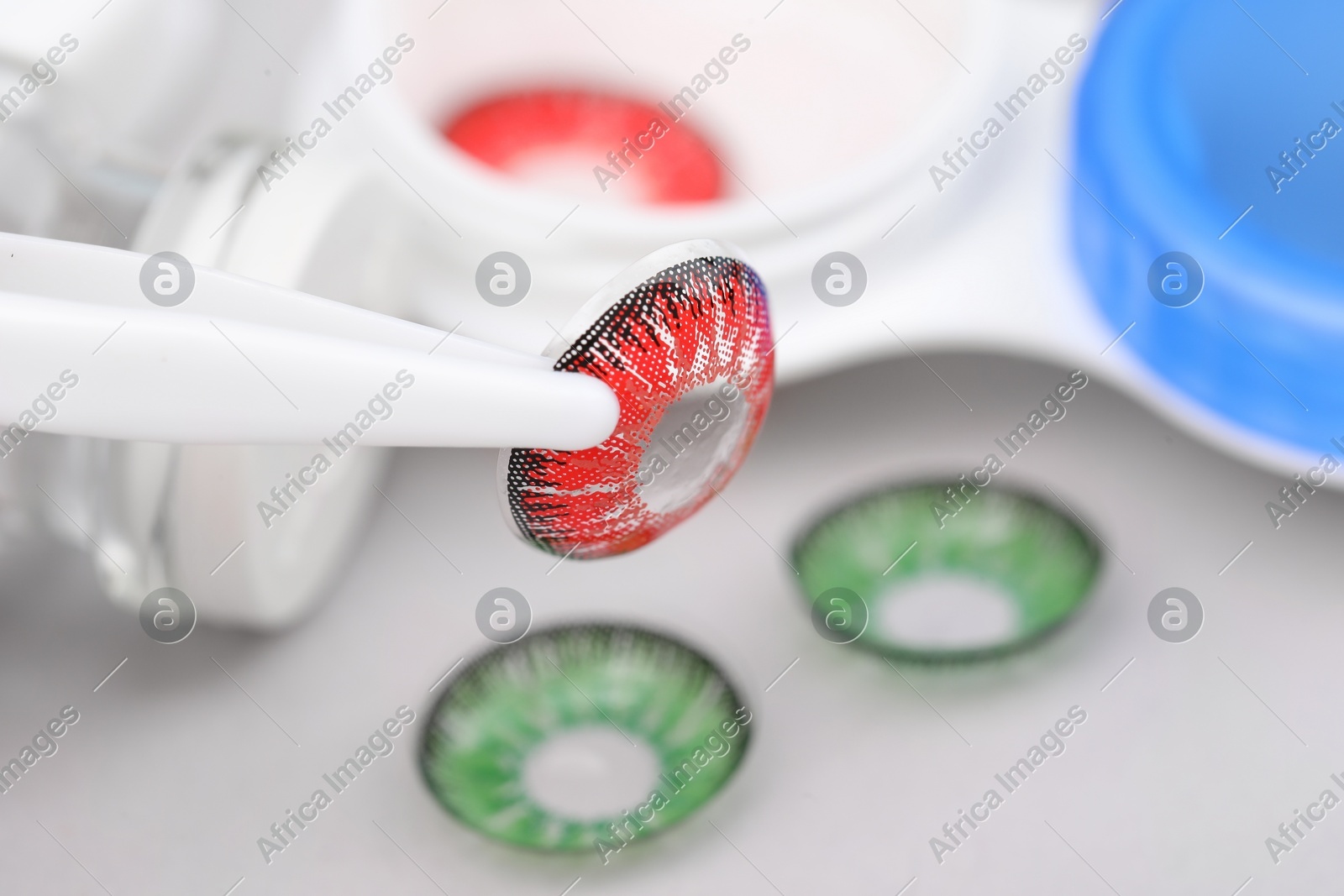 Tweezers with red contact lens on blurred background, closeup. Space for text Photo of Tweezers with red contact lens on blurred background, closeup. Space for text