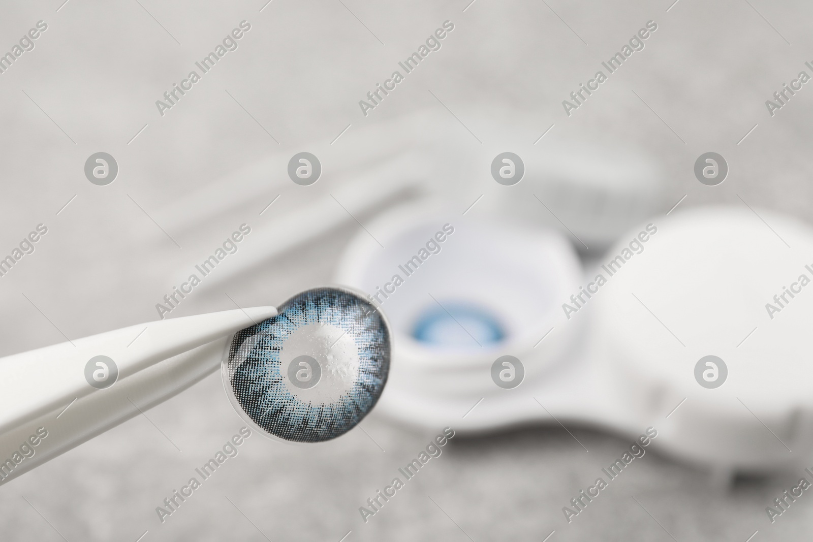 Tweezers with blue contact lens over table, closeup. Space for text Photo of Tweezers with blue contact lens over table, closeup. Space for text