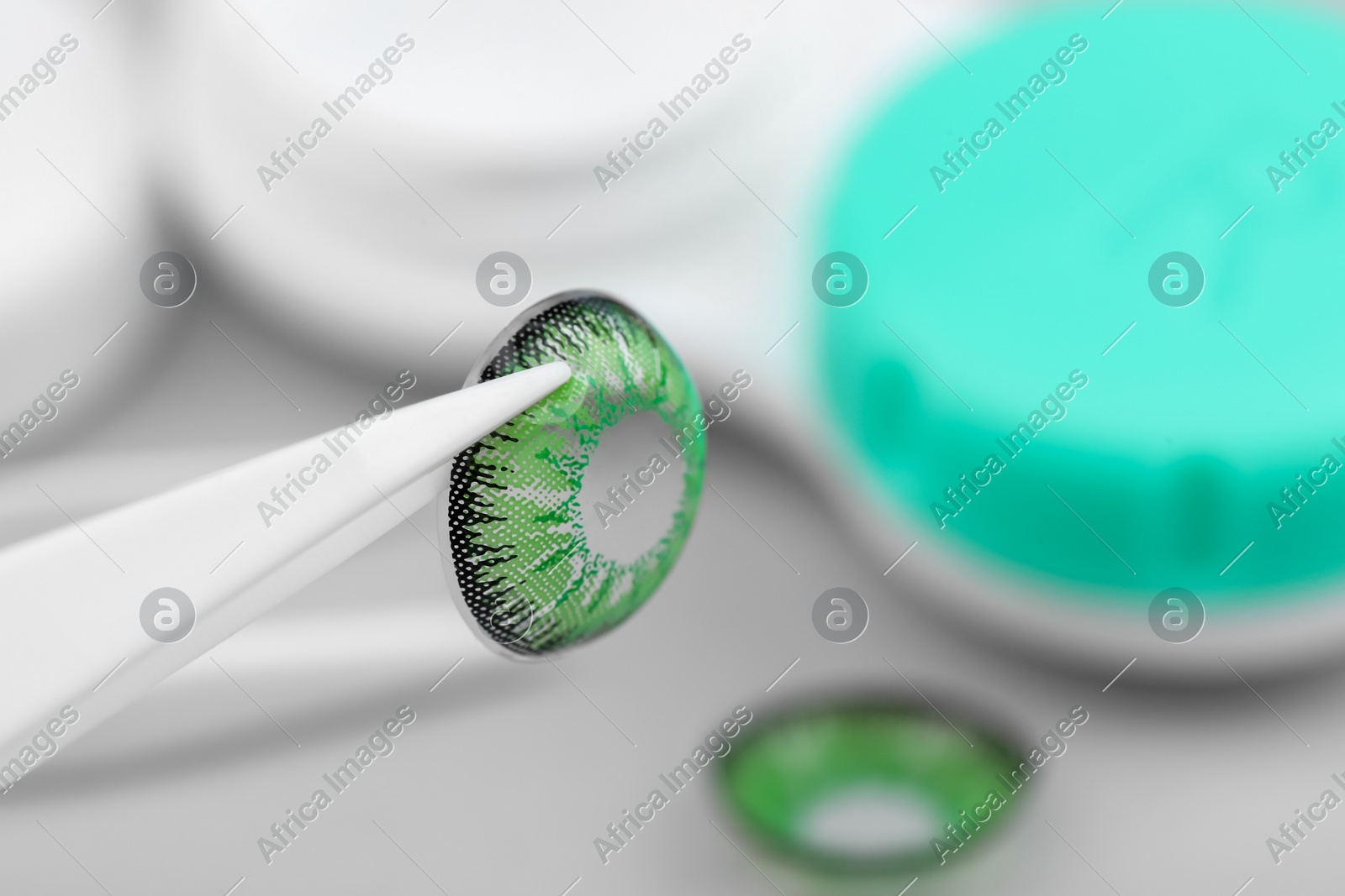 Tweezers with green contact lens on blurred background, closeup. Space for text Photo of Tweezers with green contact lens on blurred background, closeup. Space for text