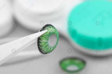 Tweezers with green contact lens on blurred background, closeup. Space for text Photo of Tweezers with green contact lens on blurred background, closeup. Space for text