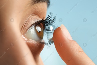 Young woman putting contact lens in her eye on light blue background, closeup Photo of Young woman putting contact lens in her eye on light blue background, closeup