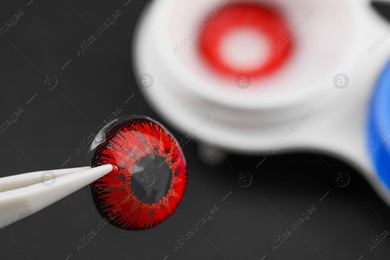 Tweezers with red contact lens on dark background, closeup. Space for text Photo of Tweezers with red contact lens on dark background, closeup. Space for text