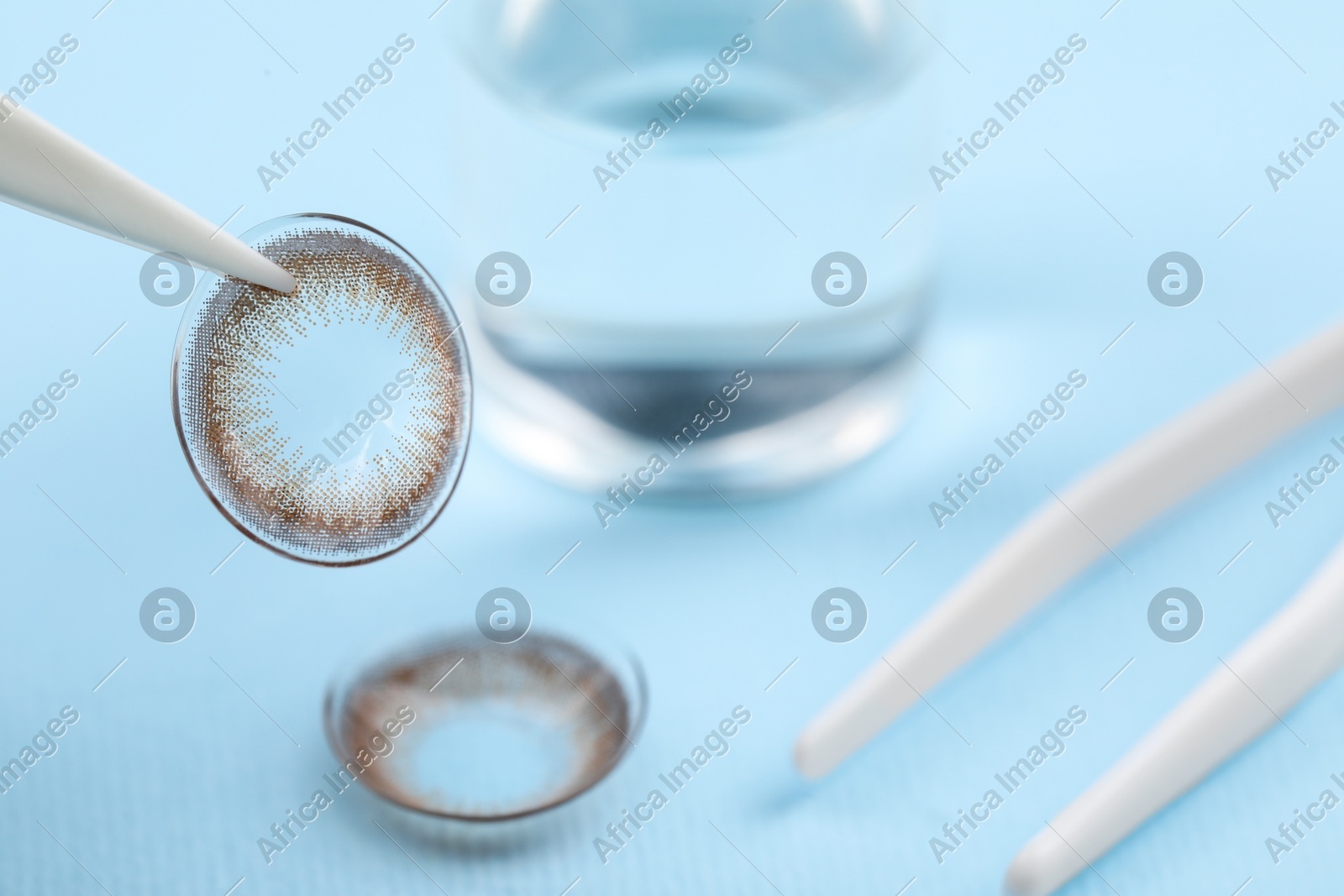 Tweezers with color contact lens on light blue background, closeup. Space for text Photo of Tweezers with color contact lens on light blue background, closeup. Space for text