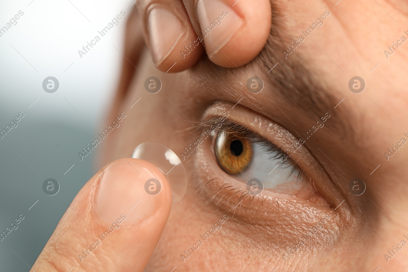 Man putting contact lens in his eye on blurred background, closeup Photo of Man putting contact lens in his eye on blurred background, closeup