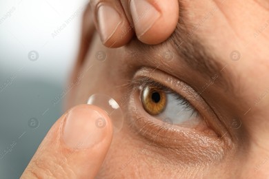 Man putting contact lens in his eye on blurred background, closeup Photo of Man putting contact lens in his eye on blurred background, closeup