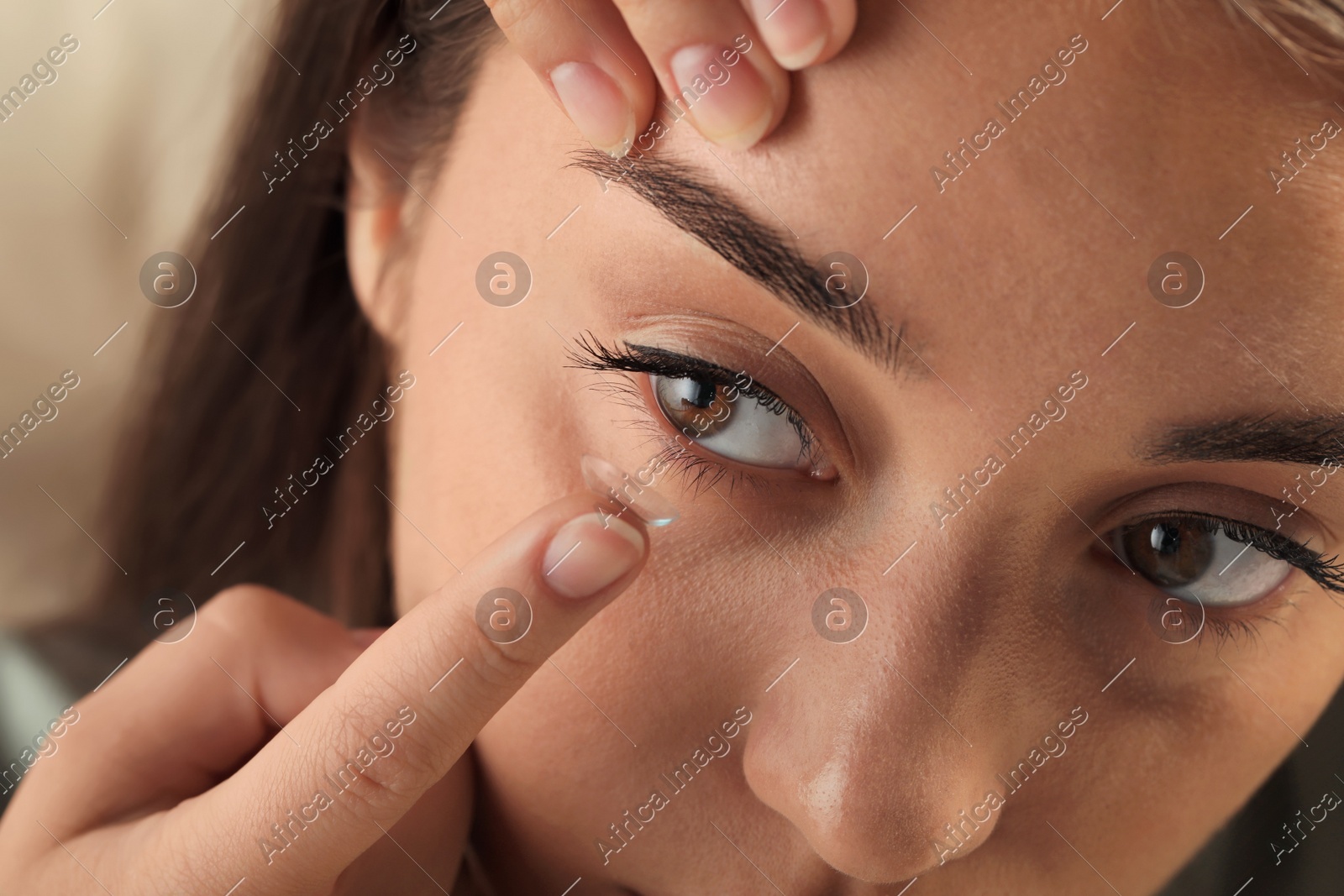 Young woman putting contact lens in her eye on blurred background, closeup Photo of Young woman putting contact lens in her eye on blurred background, closeup