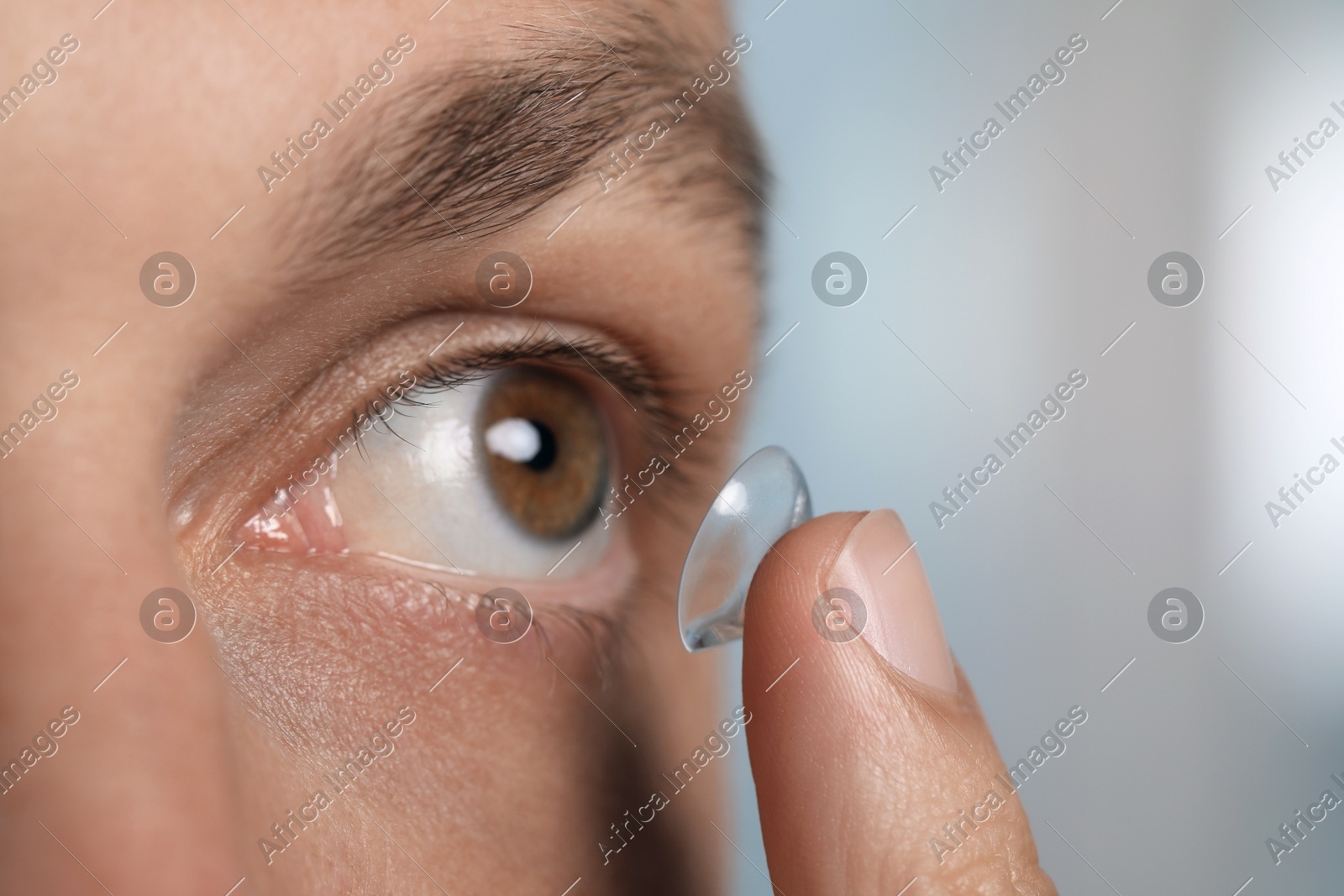 Man putting contact lens in his eye on blurred background, closeup Photo of Man putting contact lens in his eye on blurred background, closeup