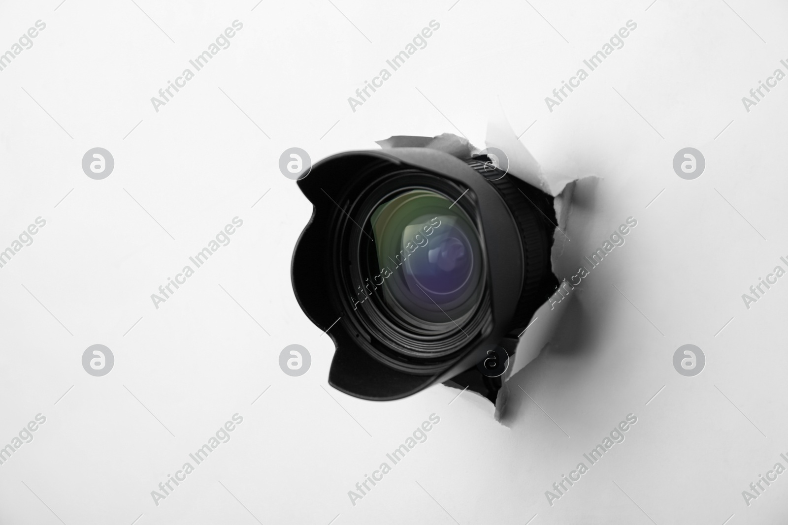 Hidden camera lens through torn hole in white paper Photo of Hidden camera lens through torn hole in white paper