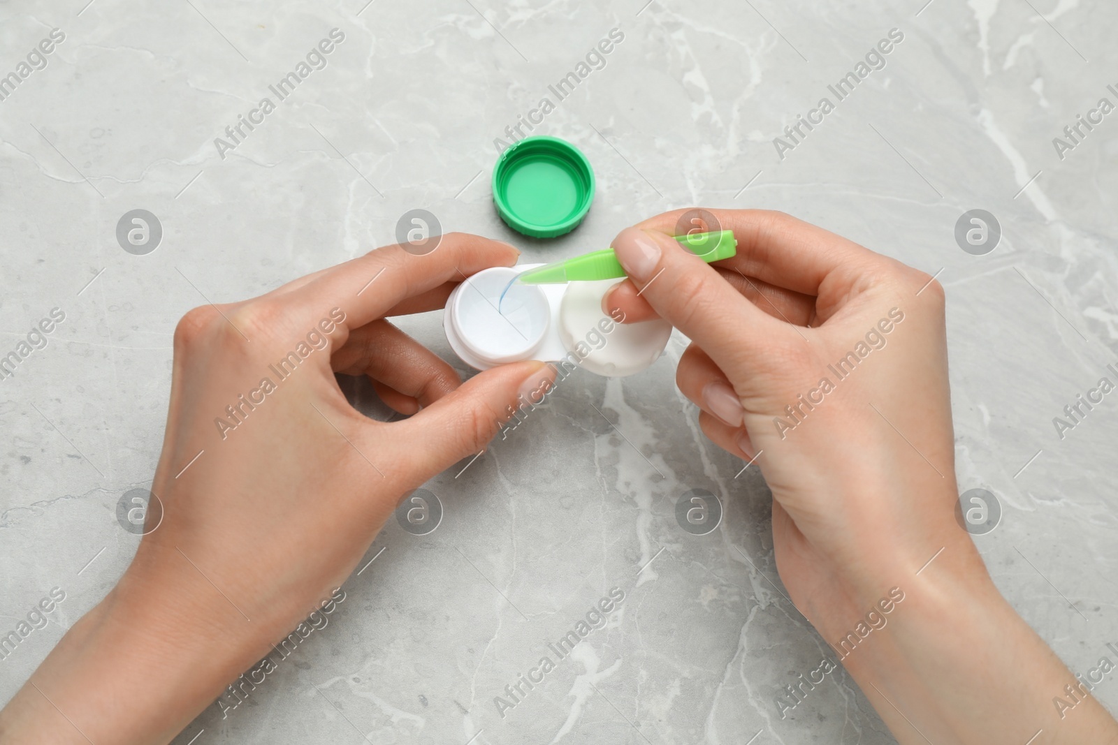 Woman taking contact lens from case with tweezers at light grey marble table, top view Photo of Woman taking contact lens from case with tweezers at light grey marble table, top view