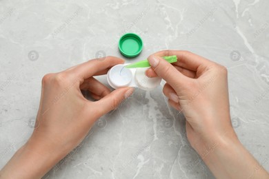 Woman taking contact lens from case with tweezers at light grey marble table, top view Photo of Woman taking contact lens from case with tweezers at light grey marble table, top view