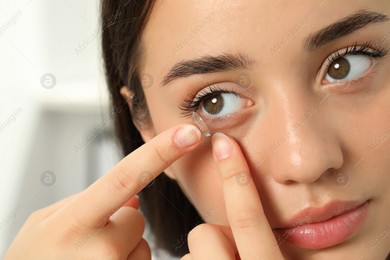 Woman putting contact lens in her eye on blurred background, closeup Photo of Woman putting contact lens in her eye on blurred background, closeup
