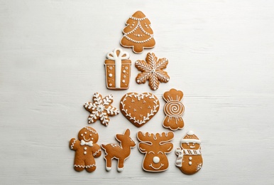 Photo of Christmas tree shape made of delicious decorated gingerbread cookies on white wooden table, flat lay