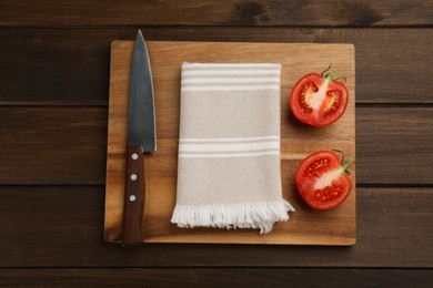Cutting board with kitchen towel, halved tomato and knife on wooden table, top view Photo of Cutting board with kitchen towel, halved tomato and knife on wooden table, top view