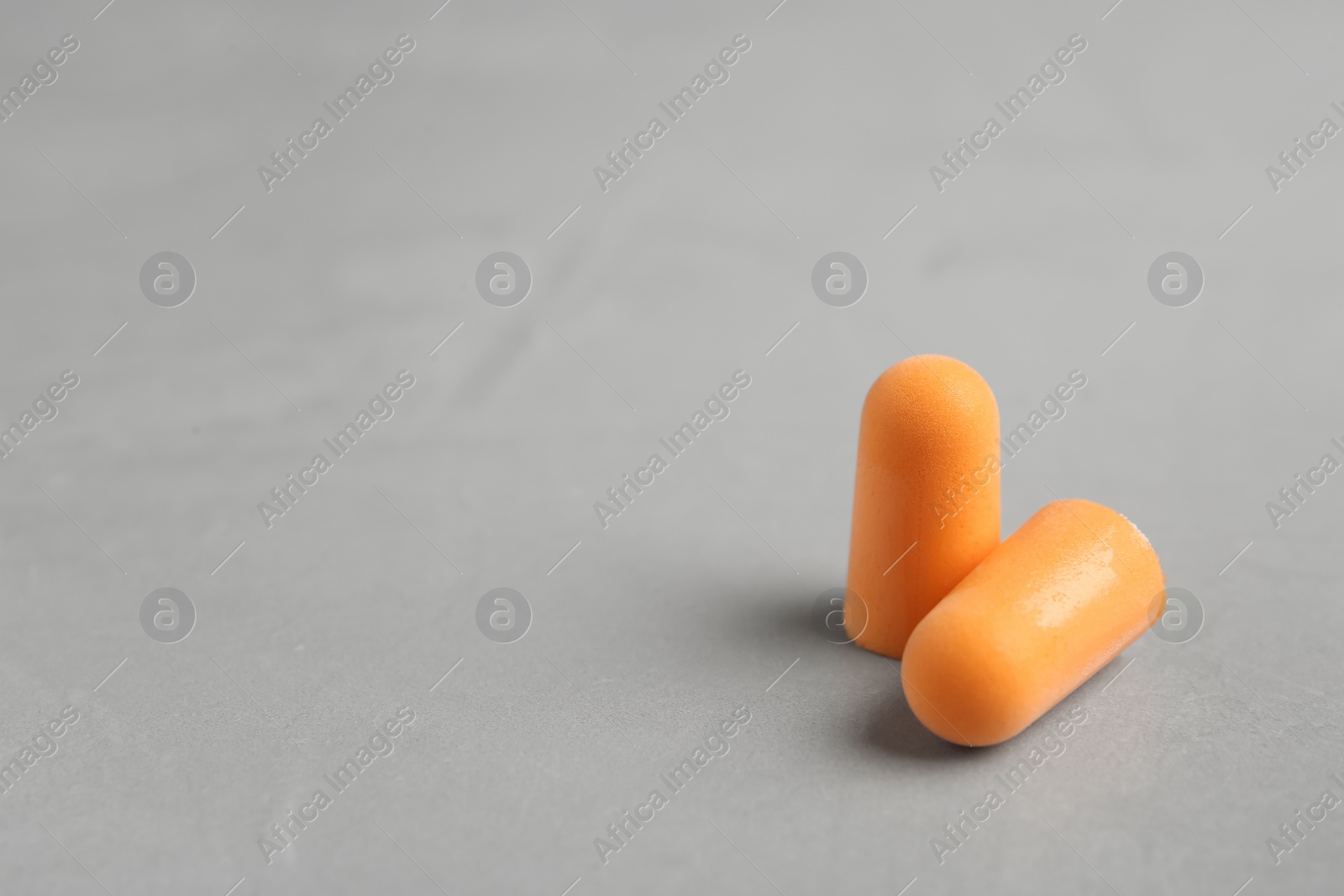 Pair of orange ear plugs on grey background. Space for text Photo of Pair of orange ear plugs on grey background. Space for text