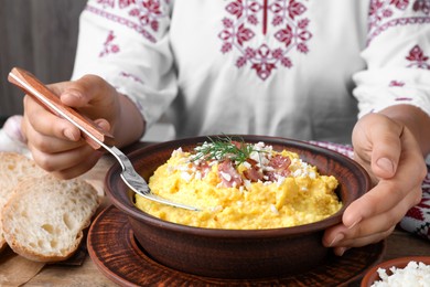 Woman eating banosh with brynza and pork cracklings at wooden table, closeup. Traditional Ukrainian dish Photo of Woman eating banosh with brynza and pork cracklings at wooden table, closeup. Traditional Ukrainian dish