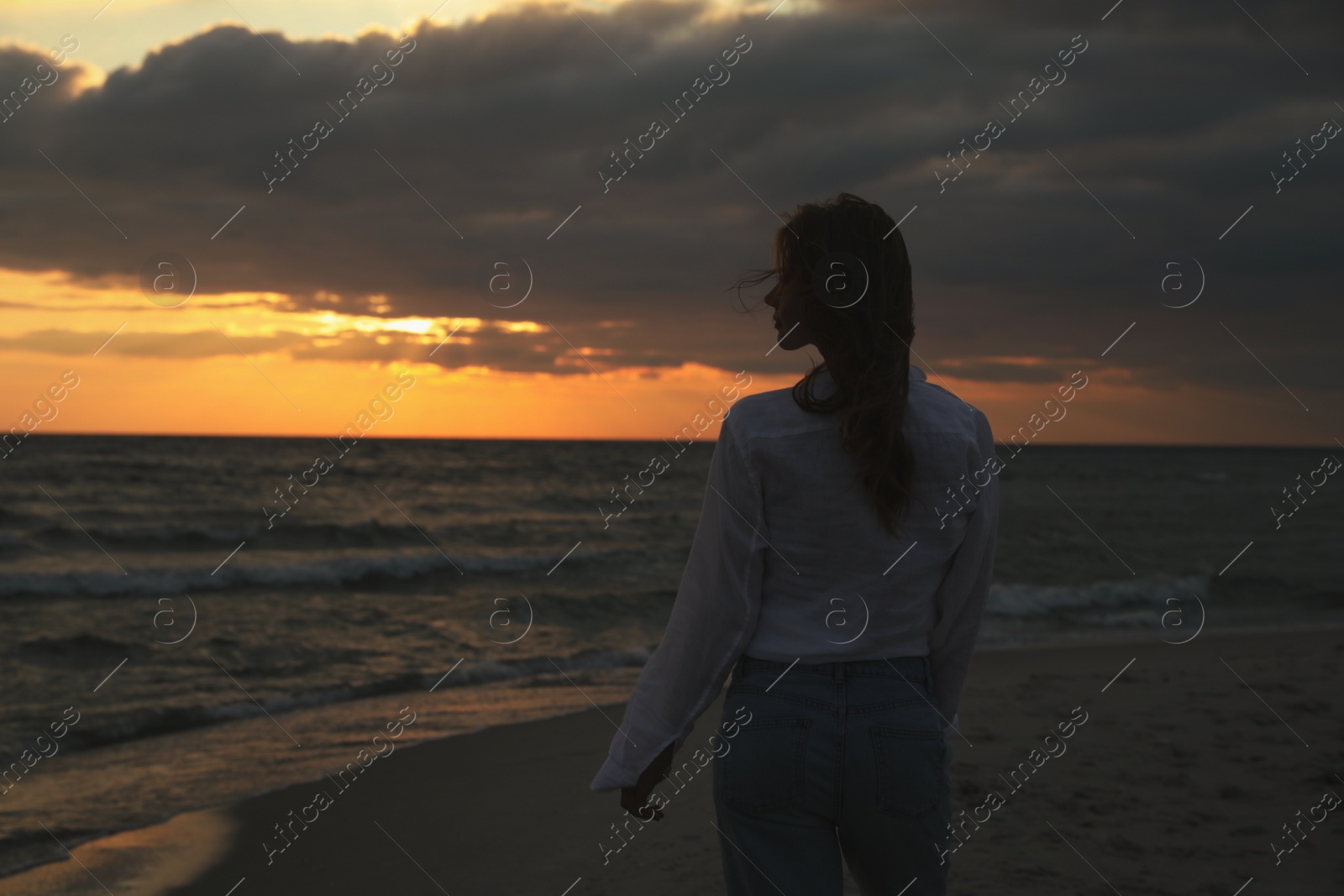 Woman on sandy beach during sunset, back view Photo of Woman on sandy beach during sunset, back view