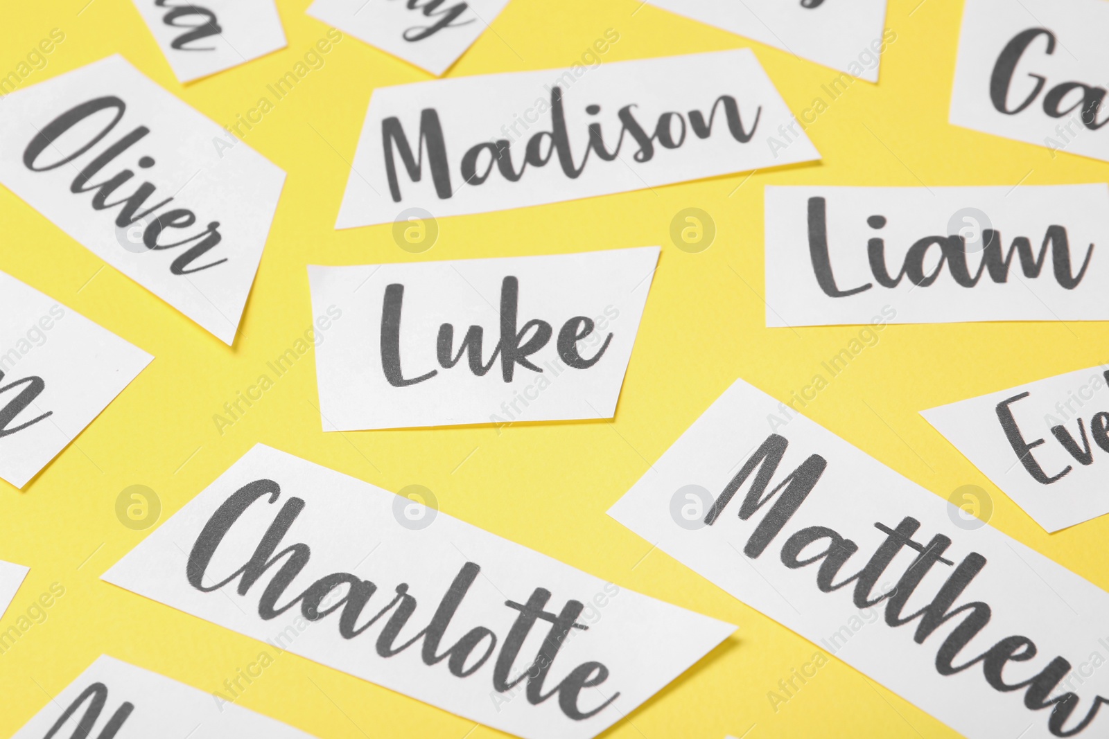 Paper sheets with written different baby names on yellow background, closeup Photo of Paper sheets with written different baby names on yellow background, closeup