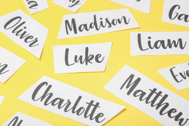 Paper sheets with written different baby names on yellow background, closeup Photo of Paper sheets with written different baby names on yellow background, closeup