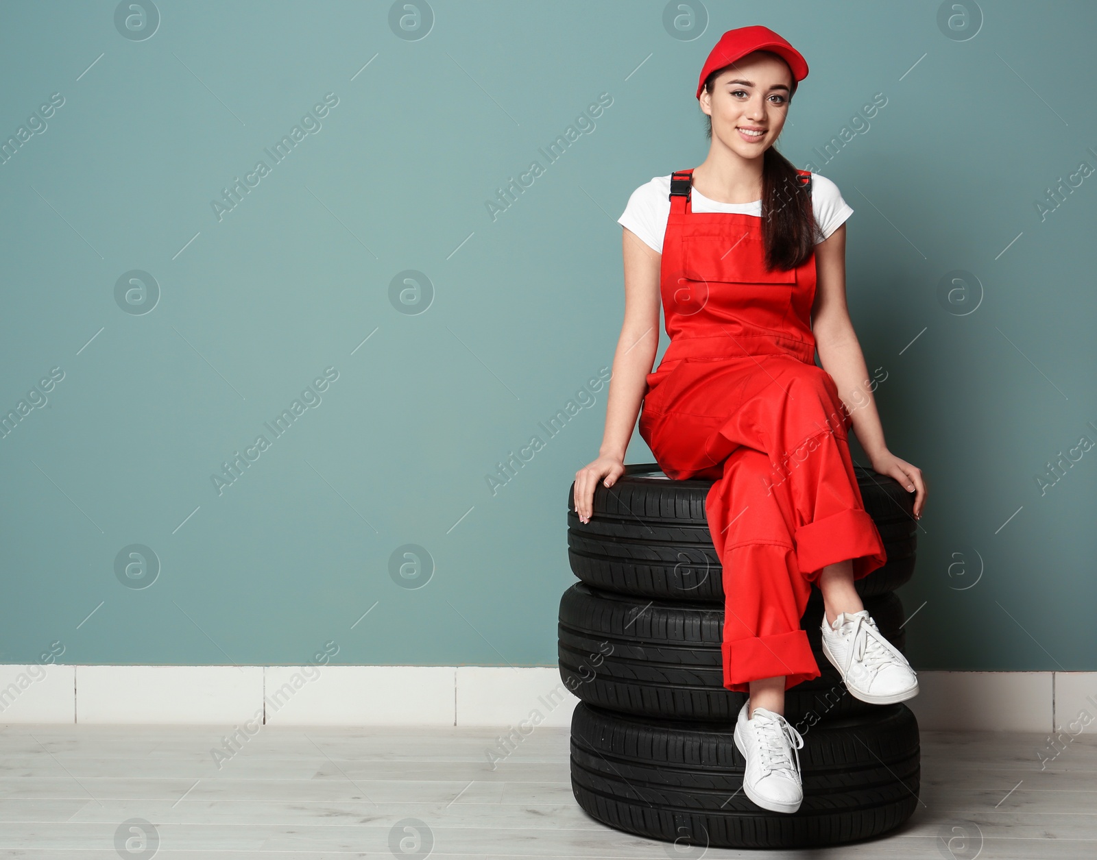 Female mechanic in uniform with car tires on color wall background Photo of Female mechanic in uniform with car tires on color wall background