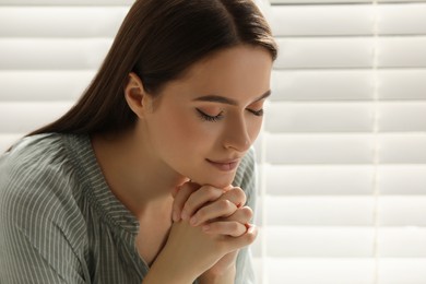 Religious young woman praying near window indoors, closeup Photo of Religious young woman praying near window indoors, closeup