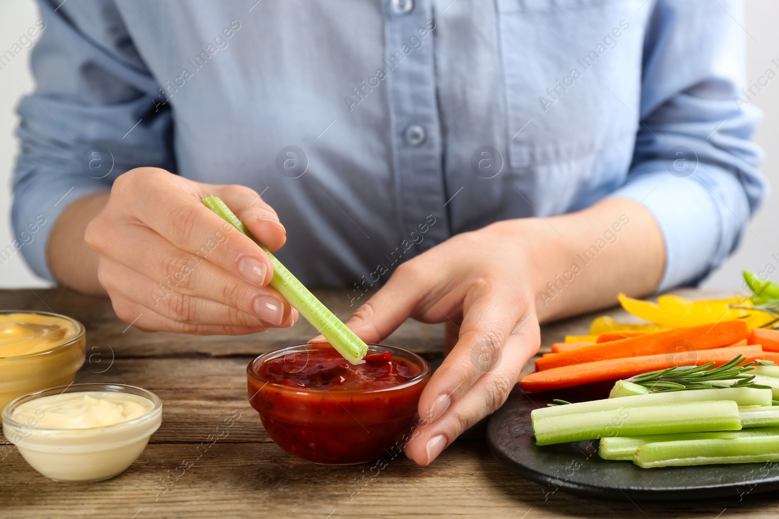 Woman dipping celery stick in sauce at wooden table, closeup Photo of Woman dipping celery stick in sauce at wooden table, closeup