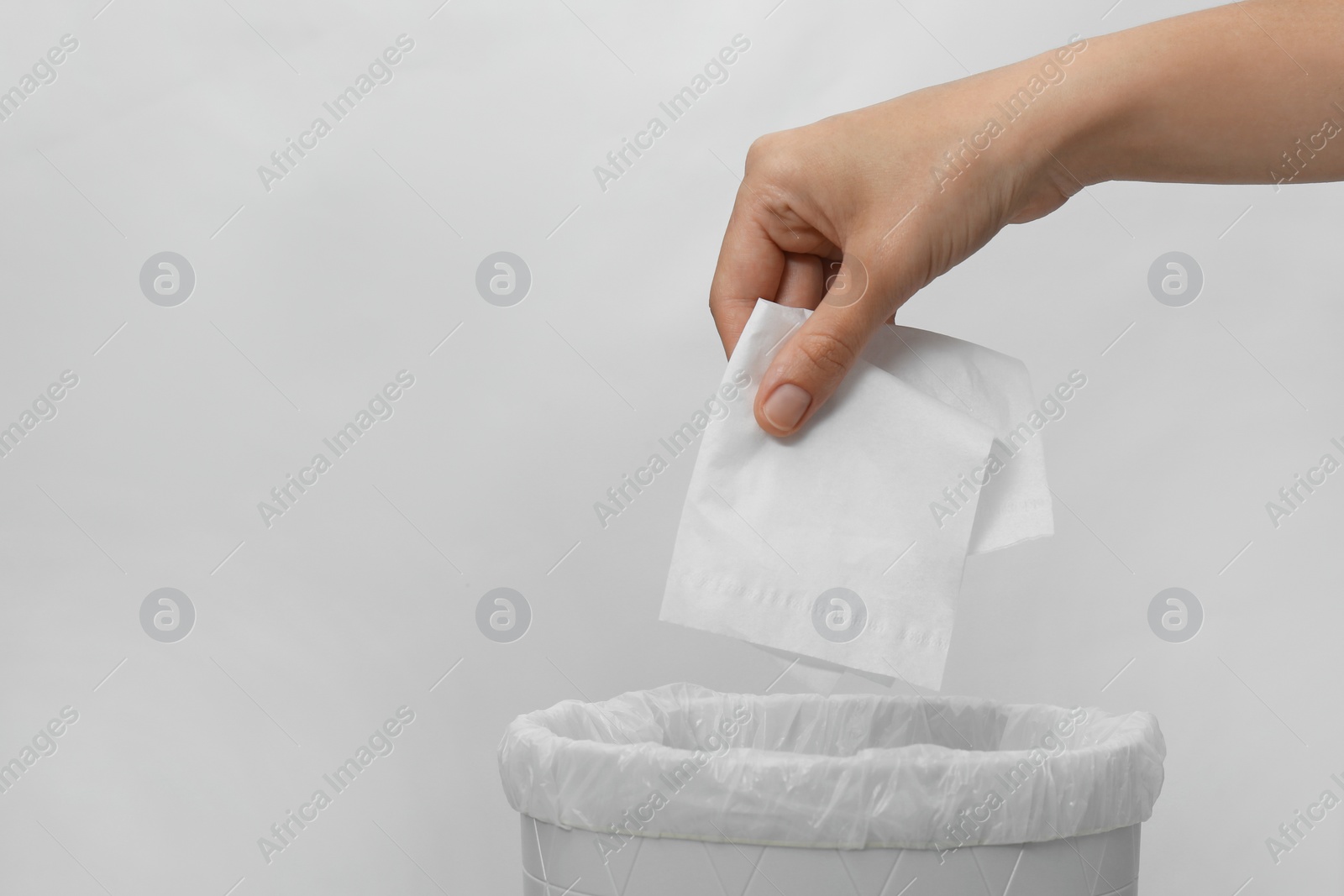 Woman putting paper tissue into trash bin on light background, closeup Photo of Woman putting paper tissue into trash bin on light background, closeup