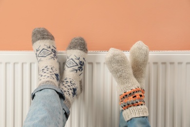 Couple warming legs on heating radiator near color wall, closeup Photo of Couple warming legs on heating radiator near color wall, closeup