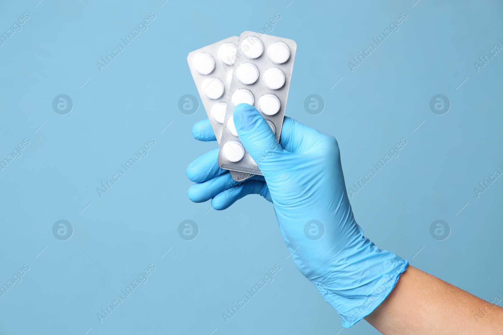 Scientist in protective gloves holding pills on light blue background, closeup Photo of Scientist in protective gloves holding pills on light blue background, closeup