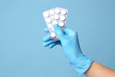 Scientist in protective gloves holding pills on light blue background, closeup Photo of Scientist in protective gloves holding pills on light blue background, closeup