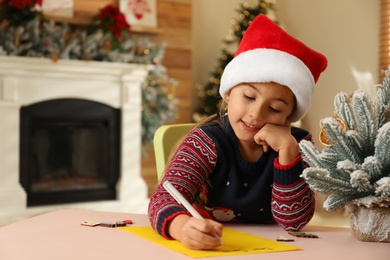 Cute child writing letter to Santa Claus at table indoors. Christmas tradition Photo of Cute child writing letter to Santa Claus at table indoors. Christmas tradition