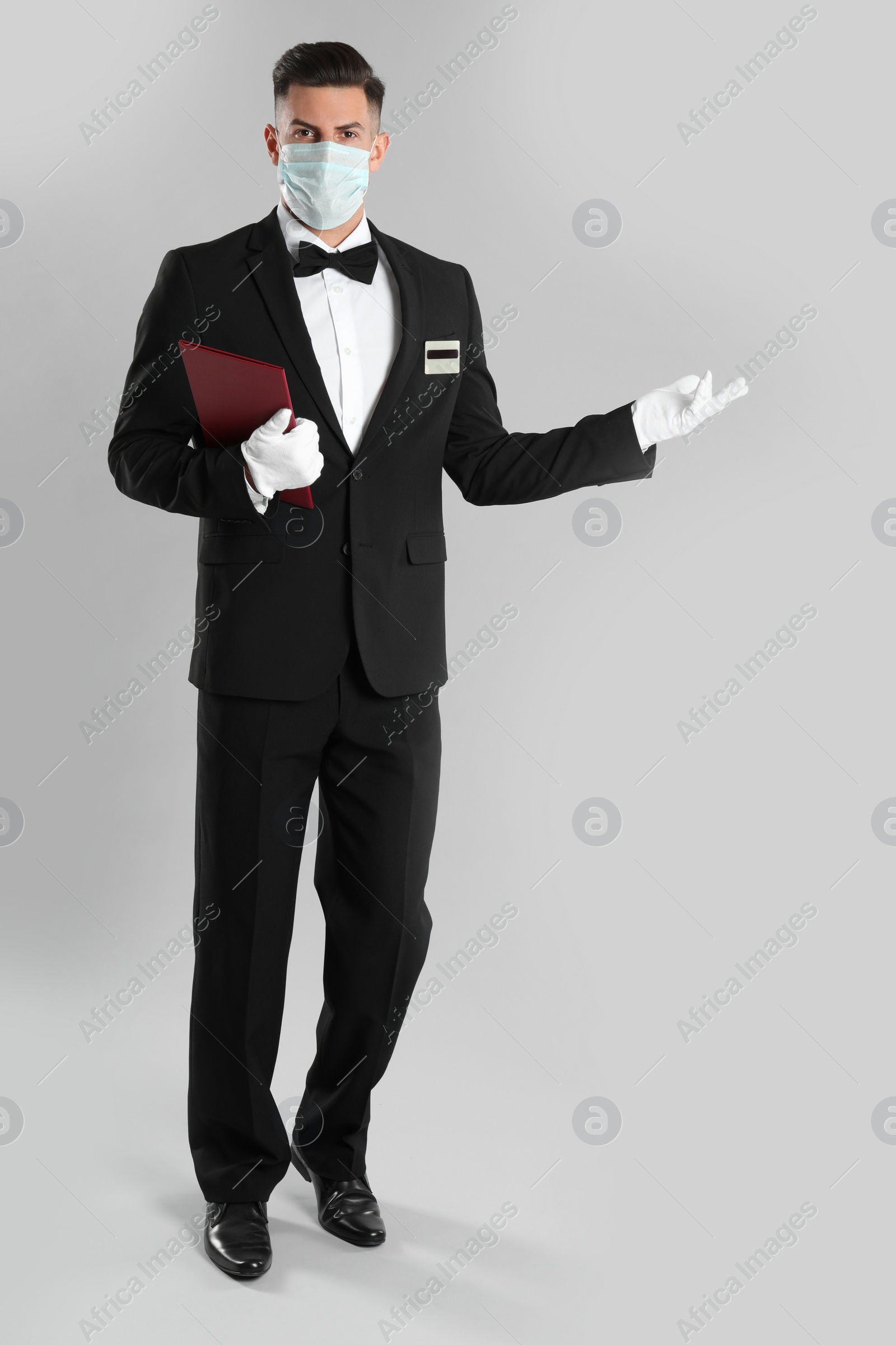 Waiter in medical face mask with menu on light grey background Photo of Waiter in medical face mask with menu on light grey background