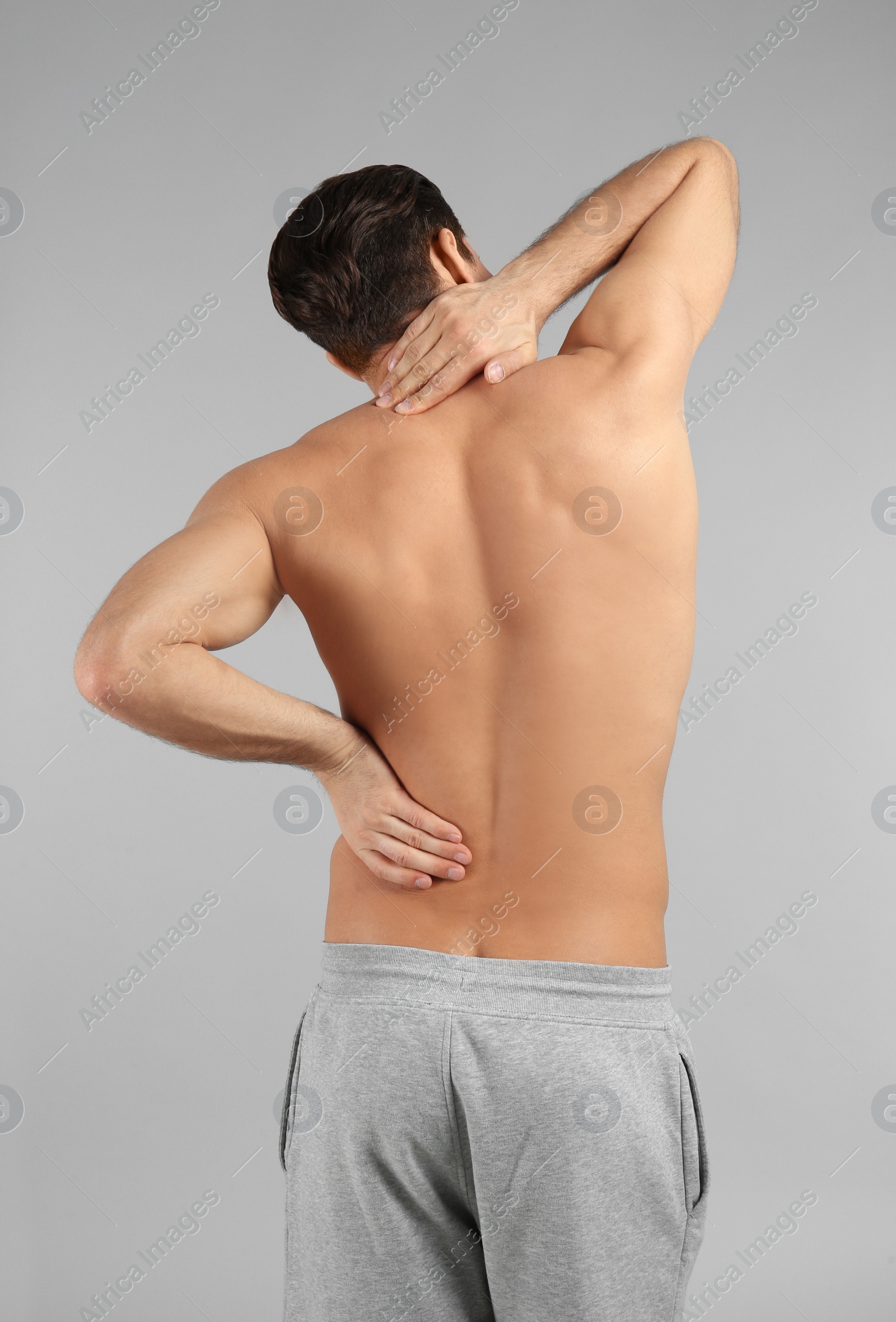 Young man suffering from back pain on grey background Photo of Young man suffering from back pain on grey background