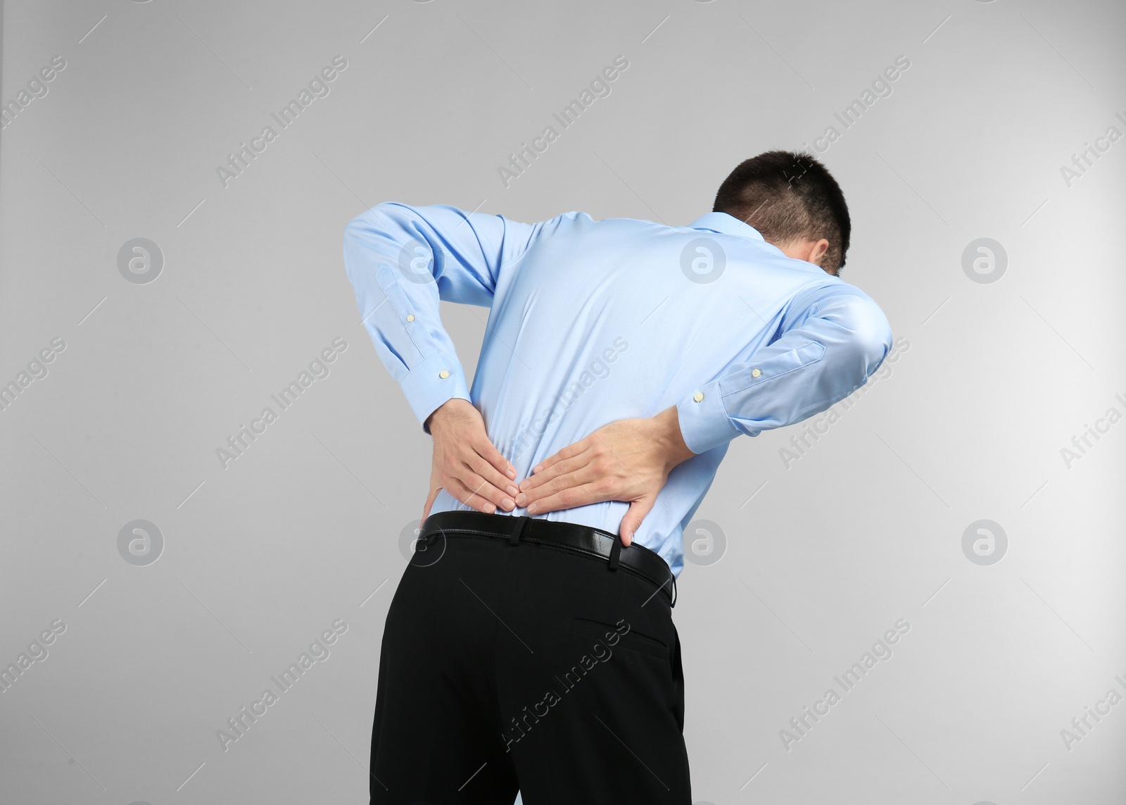 Young man suffering from back pain on light background Photo of Young man suffering from back pain on light background