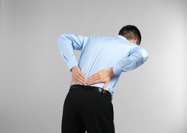 Young man suffering from back pain on light background Photo of Young man suffering from back pain on light background